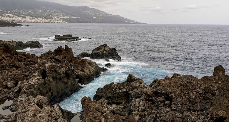 Costa rocosa con olas rompiendo y un pueblo distante.