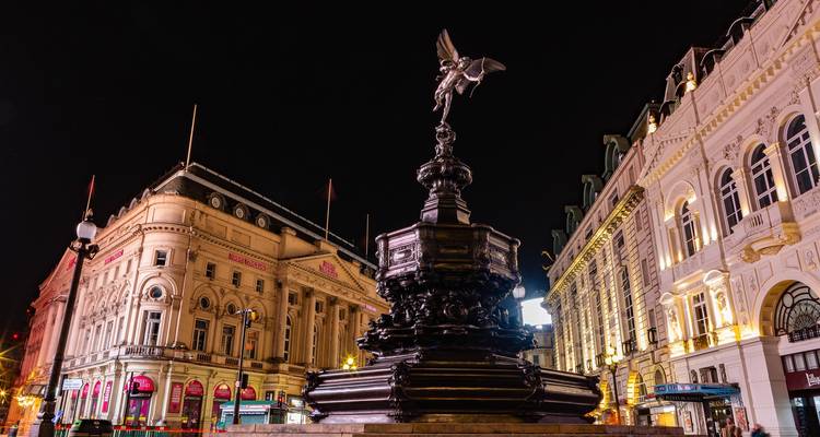 City square at night with illuminated buildings and a statue.