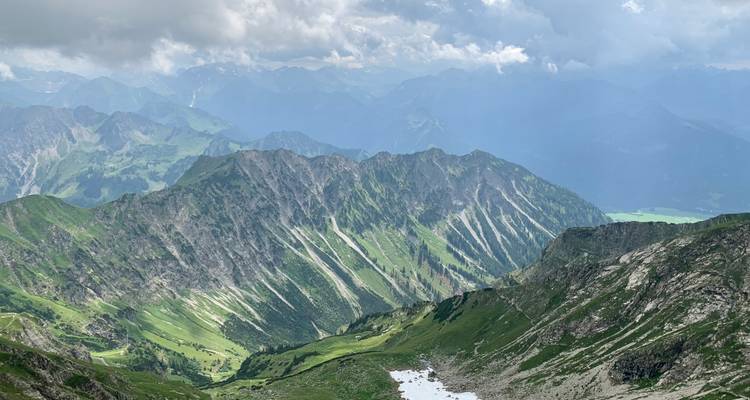Mountain peaks under a cloudy sky, with valleys covered in greenery.