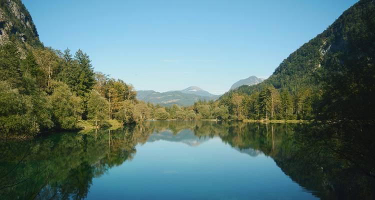 Een serene meer omringd door weelderige bergen onder een heldere blauwe hemel.