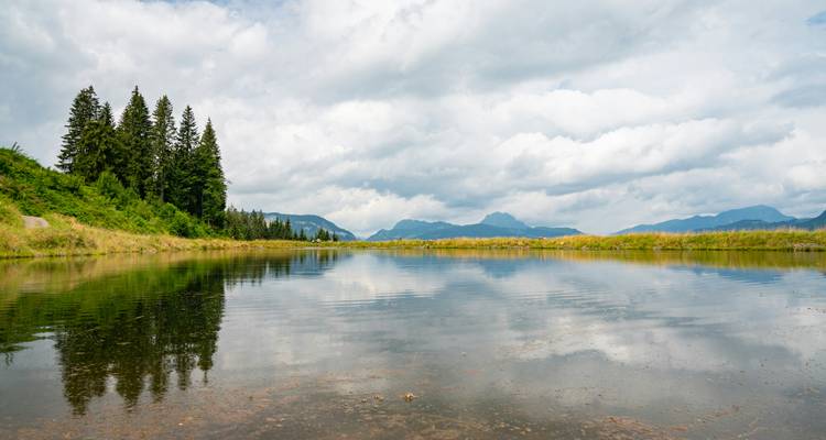 Een rustig meer met reflecties van de omringende bergen en bewolkte lucht.