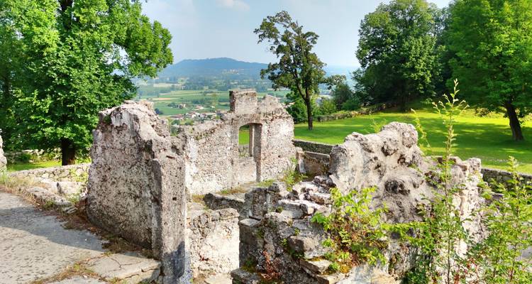 Stenen ruïnes van een oud gebouw omringd door groene velden en verre heuvels onder een deels bewolkte hemel.