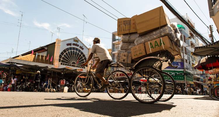 Persona transportando mercancías en un rickshaw en una zona de mercado bulliciosa.