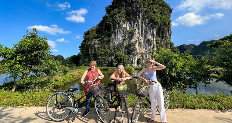 Three women with bicycles in front of a limestone cliff.