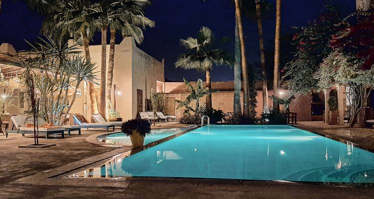 Une vue nocturne d'un espace piscine magnifiquement éclairé entouré de palmiers.