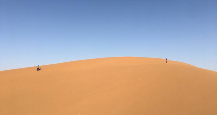 Deux personnes au sommet d'une dune de sable dans un vaste désert.