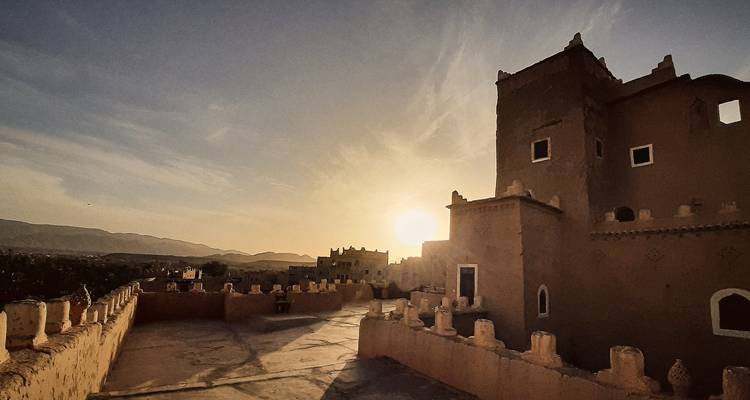 Coucher de soleil sur un bâtiment traditionnel du désert avec des montagnes en arrière-plan.