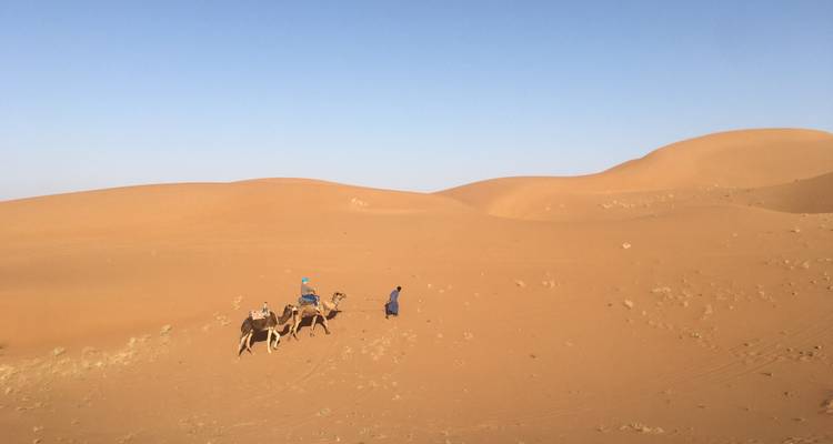 Deux personnes et des chameaux traversant des dunes de sable dans un désert.