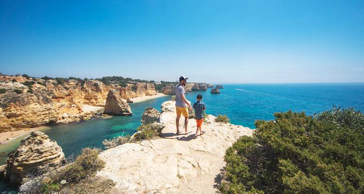 Homme et enfant debout sur une falaise surplombant la plage et la mer.