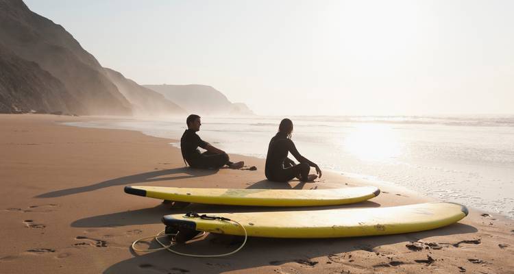 Deux personnes assises sur le sable avec des planches de surf à côté d'elles.