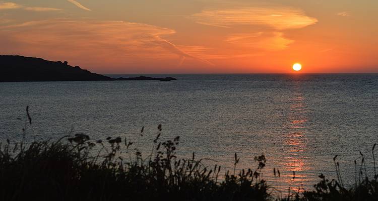 Soleil se couchant sur l'océan avec un littoral en silhouette.