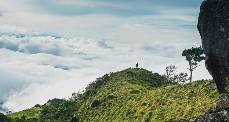 Personne debout sur un sommet herbeux au-dessus des nuages.