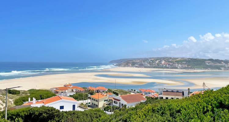Vue côtière avec des plages de sable et des maisons sous un ciel bleu.