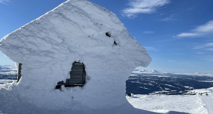 A snow-covered cabin in a mountainous winter landscape.