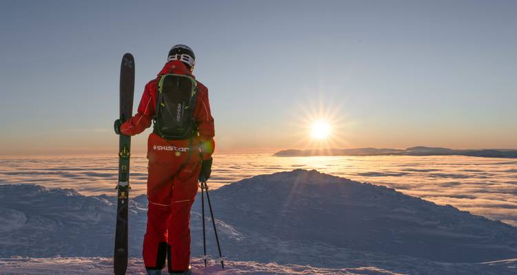 Skier standing on a snowy mountain peak looking at a sunset.