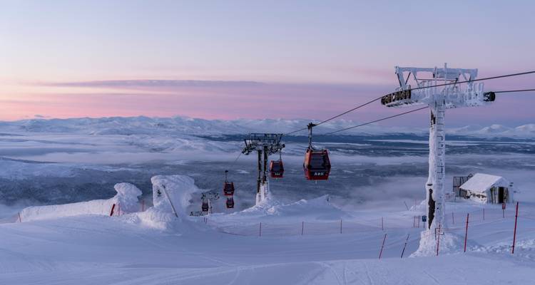 Ski lift with gondolas over snow-covered landscape during sunset.