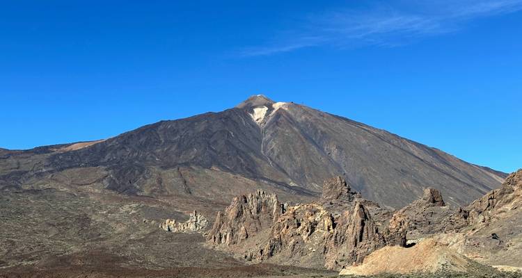 Ein vulkanischer Berg mit zerklüftetem Gelände vor einem klaren blauen Himmel.