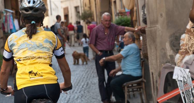 Cycliste dépassant des habitants dans une rue pavée étroite.