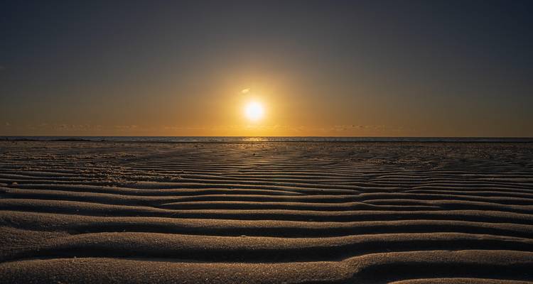 Sunrise over a sandy beach with wave patterns.