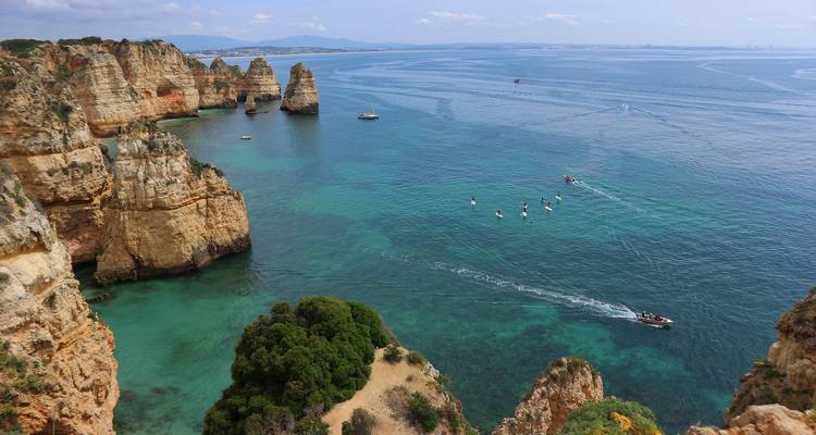 Côte spectaculaire avec formations rocheuses et bateaux dans une eau turquoise.