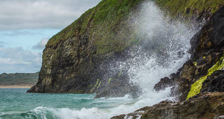 Wave crashing against a cliff with vibrant greenery.