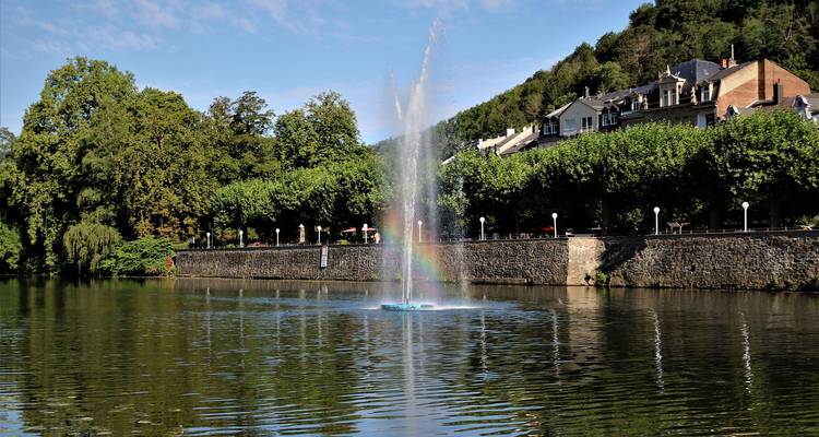 Une fontaine dans un lac avec des arbres et une promenade en arrière-plan.