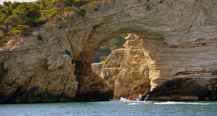 Bateau avec des personnes naviguant à travers une arche rocheuse naturelle.