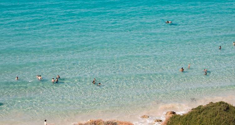 People swimming in turquoise waters near a sandy beach.