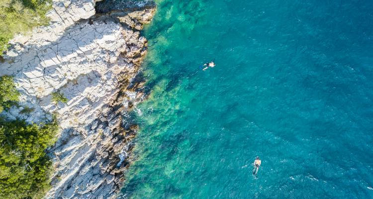 Aerial view of people swimming in deep blue waters near a rocky coastline.