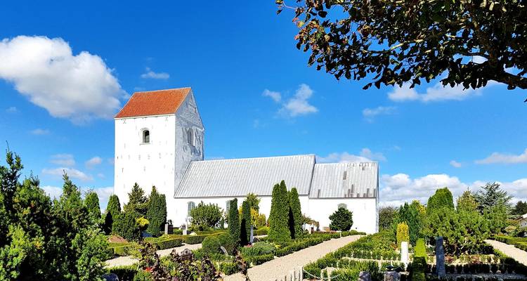 White church with a red roof amidst a lush garden.