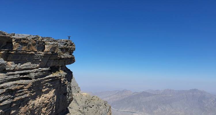 Person standing on a cliff with panoramic mountainous views.