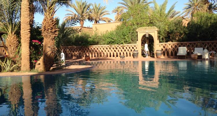 Una piscina de complejo turístico marroquí rodeada de palmeras en un entorno sereno.