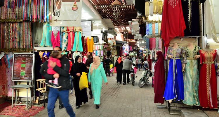 Vibrant market scene with colorful Moroccan garments and people shopping.
