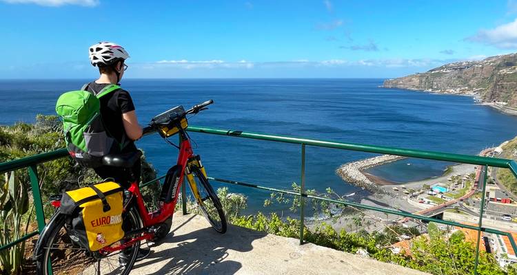 Un cycliste contemplant un paysage côtier avec les eaux bleues de l'océan sous un ciel dégagé.