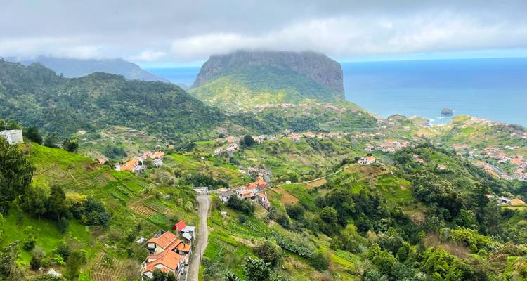 Vue aérienne d'un village côtier au milieu de collines luxuriantes sous un ciel nuageux.
