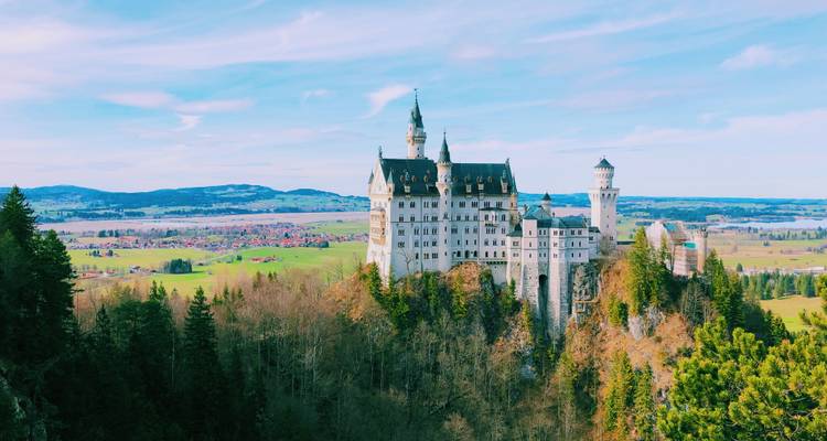 Schloss Neuschwanstein, eingebettet oberhalb eines Waldes mit Feldern in der Ferne.