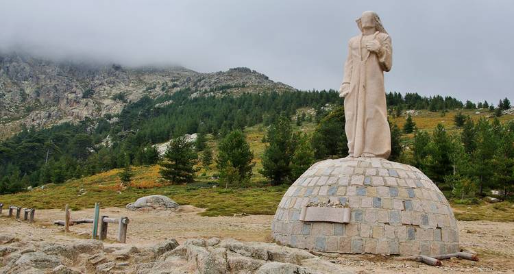 Statue en pierre sur un piédestal avec des montagnes en arrière-plan.