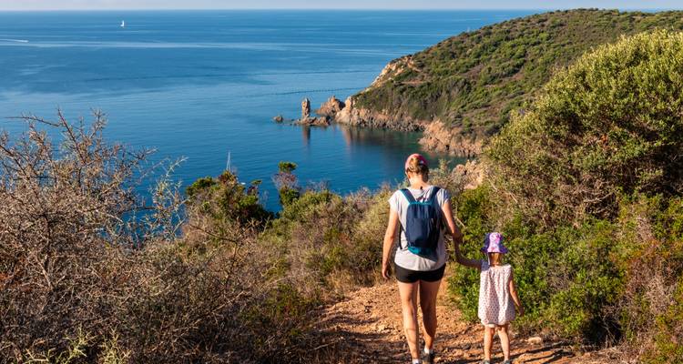 Femme et enfant descendant un sentier avec vue sur la mer et les falaises.