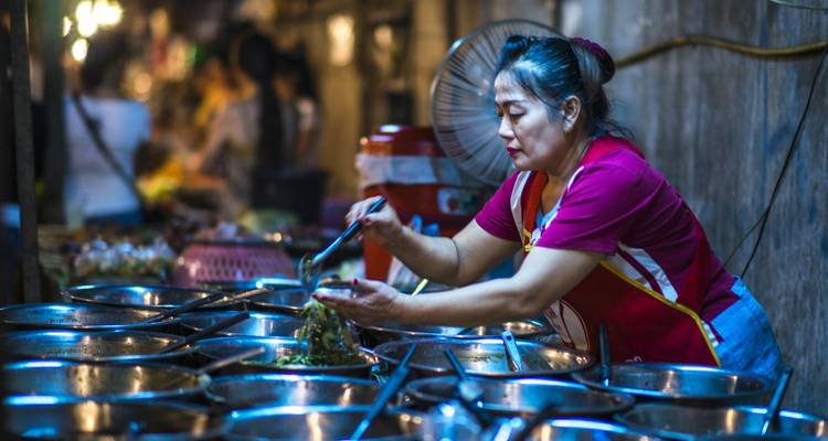Une femme servant de la nourriture à partir de grandes marmites dans un marché animé.