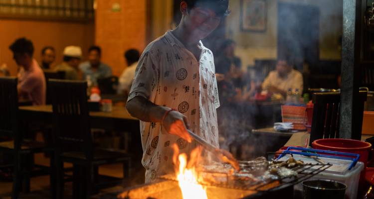Une personne qui fait griller de la nourriture dans un restaurant avec des gens qui dînent en arrière-plan.