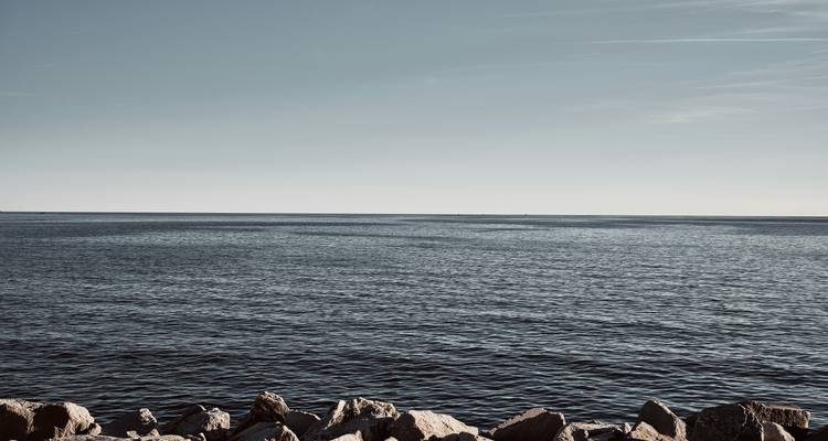 Weite Sicht auf das Meer mit Felsen im Vordergrund.