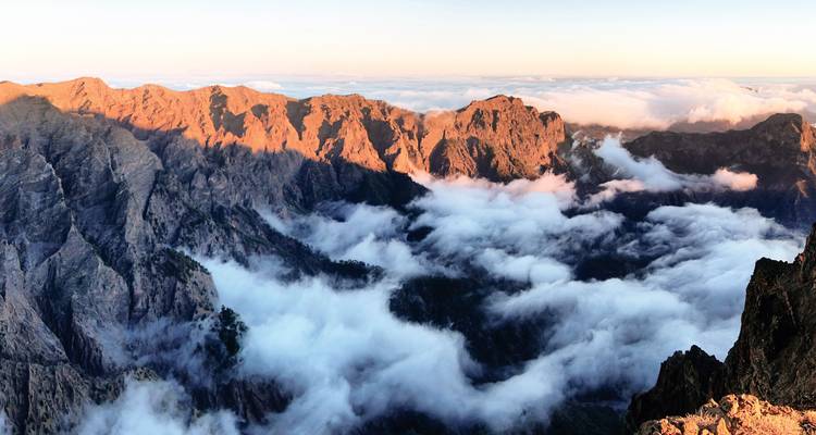 Vue montagneuse avec des nuages nichés entre les sommets au lever du soleil.