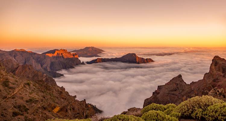 Vista expansiva de montañas sobre las nubes al amanecer.