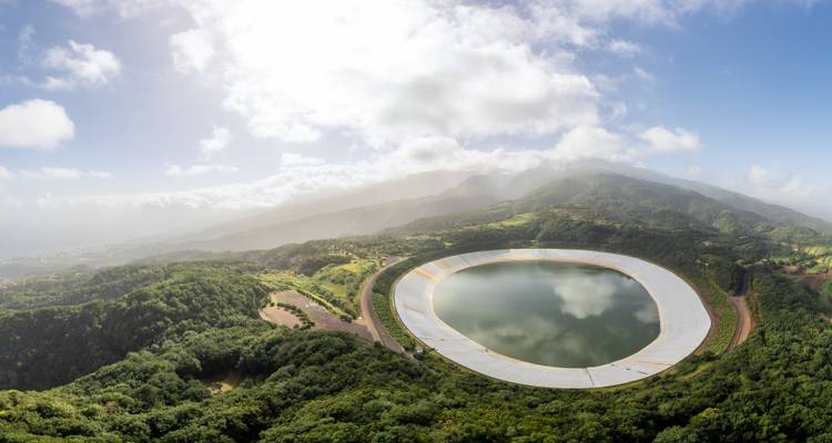 Un embalse circular rodeado de exuberantes colinas boscosas verdes.