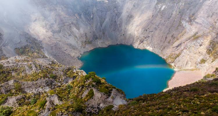 Vue aérienne d'un lac de cratère bleu profond dans un paysage volcanique.