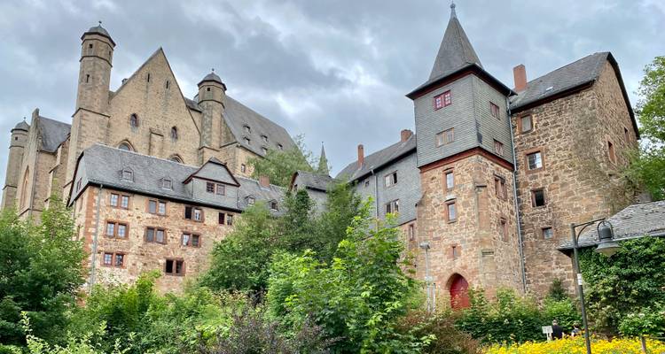 Außenansicht von Schloss Marburg mit Garten und bewölktem Himmel.