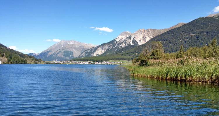 Ein ruhiger See mit Bergen und einem kleinen Dorf in der Ferne.
