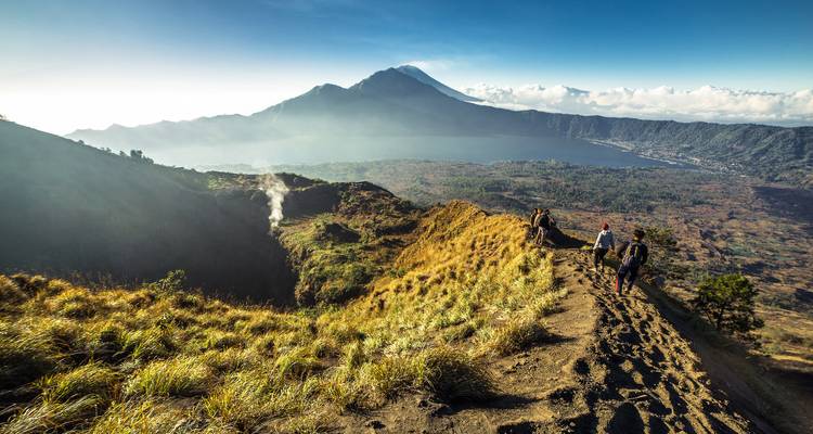 People hiking along a mountain ridge with a volcano and lake view.