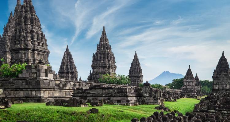 Ancient stone temple with conical spires and a mountain backdrop.