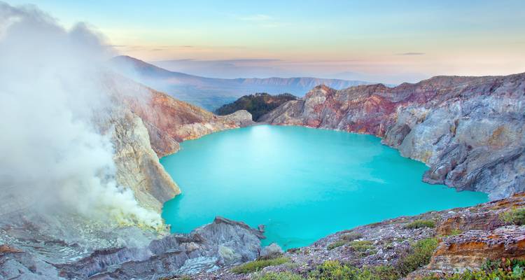 Crater lake with turquoise water surrounded by rugged cliffs at sunrise.
